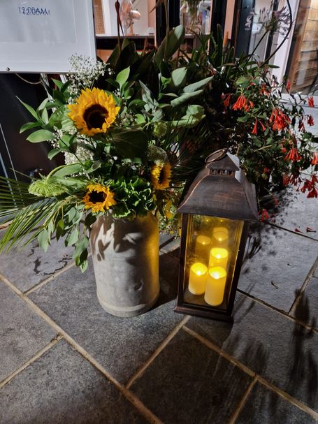 Sunflowers in a stone vase next to a lantern with candles inside
