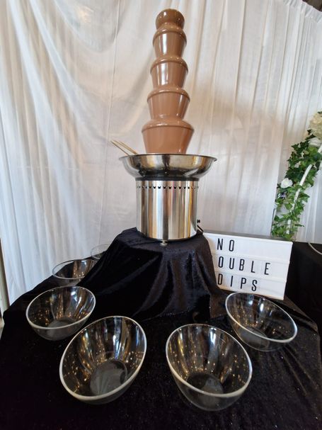A chocolate fountain surrounded by by pots ready for marshmallows and strawberries.